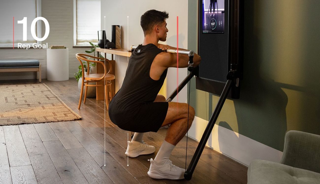 A man is working out in his living room. He is facing Tonal and completing a Barbell Front Squat.