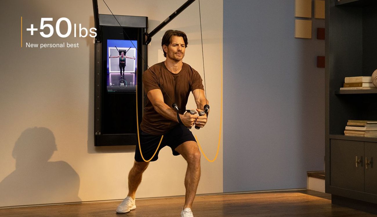 A man is working out in his living room. He is facing away from Tonal, completing a Decline Chest Fly.