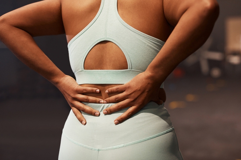 Woman in workout clothes holding her back in pain