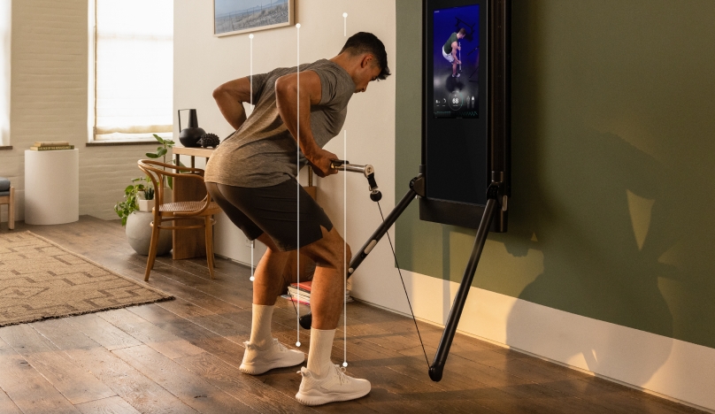 A man is working out in his living room. He is facing Tonal, completing a Barbell Bent Over Row.