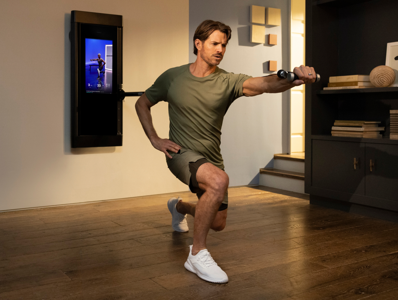 A man is working out in his living room. He is facing away from Tonal, completing an Iso Chest Split Squat.